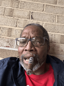 a man wearing glasses and a red shirt smoking a cigar