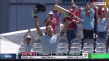 a man is holding a cricket bat over his head in front of a crowd and a sky sports advertisement