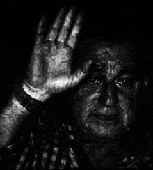 a man in a plaid shirt is covering his face with his hand in a black and white photo .