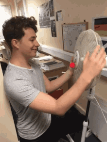 a man is adjusting a fan in front of a white board that says ' i 'm not a fan '