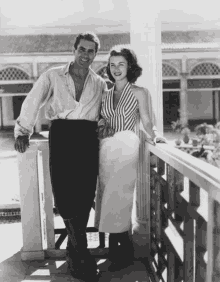 a black and white photo of a man and woman standing next to each other on a balcony