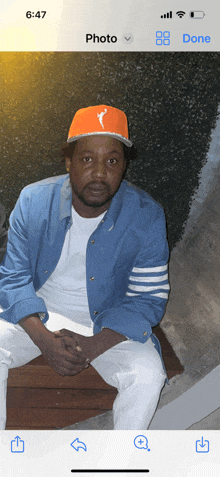 a man wearing an orange hat is sitting on a bench in front of a phone screen that says photo