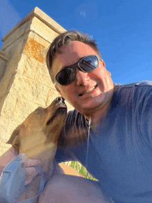 a man wearing sunglasses holds a brown dog in his lap