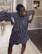 a woman in a striped dress is dancing in a living room with a small dog in the background