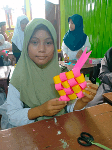 a girl in a green hijab holds a pink and yellow item