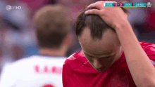 a man in a red shirt holds his head during a soccer game between den and england