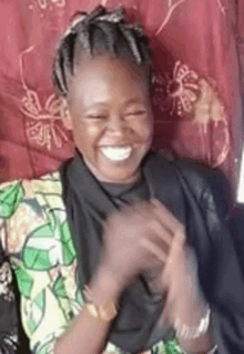 a woman is smiling and clapping her hands while sitting in front of a curtain .