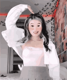 a girl in a pink tank top and a white jacket is making a heart shape with her hand in her hair .