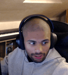 a man wearing headphones looks at the camera with a keyboard in the background