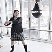 a girl in a school uniform is standing in front of a punching bag with the word banned on it .