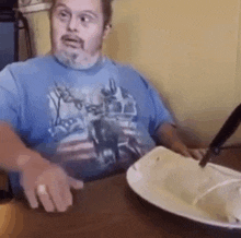 a man with down syndrome is sitting at a table with a plate of food and a knife .