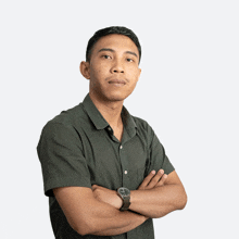 a man in a green shirt has his arms crossed and a watch on