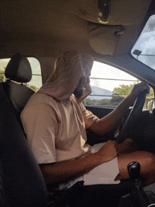 a man driving a car with a towel over his head