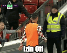 a man in an orange shirt is standing next to a man in a yellow vest with the words izin off written on the bottom