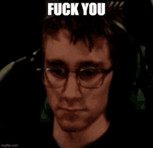 a close up of a man wearing glasses and headphones with the words `` fuck you '' written on his face .