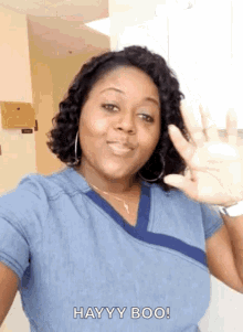 a woman in a blue scrub top is waving her hand and says hayy boo .