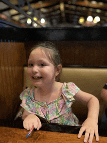 a little girl is sitting at a table with a pencil in her hand