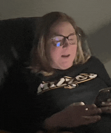 a woman wearing glasses is sitting in a chair and looking at her cell phone