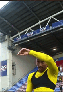 a man in a yellow shirt is standing in front of a stadium with a sign that says vv on it