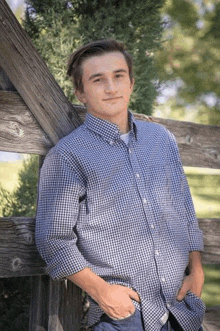 a young man in a plaid shirt is standing next to a wooden fence .