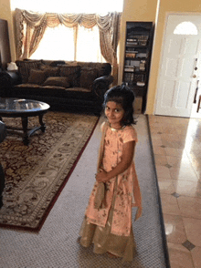 a little girl in a pink dress stands in front of a living room