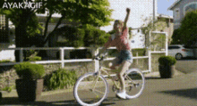 a woman is riding a bike down a street with her arm in the air and the words ayakagif above her