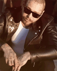 a man wearing sunglasses and a leather jacket has a tattoo on his forehead