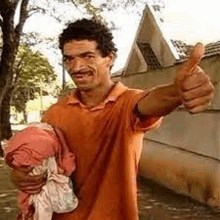 a man in an orange shirt is giving a thumbs up while holding a bag of clothes .