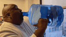 a man is drinking from a large blue bottle