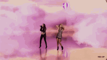 two women are singing and dancing in front of a pink cloudy sky