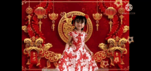 a little girl in a red and white dress is standing in front of a red background with lanterns .