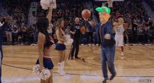 a man holding a basketball stands on a basketball court with cheerleaders and the number 00