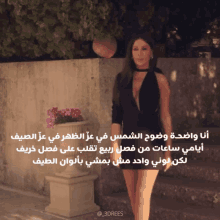 a woman in a black dress is standing in front of a wall with arabic writing on it