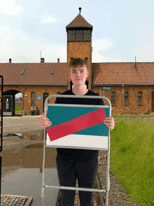 a young man holds a folding chair with a red white and blue stripe on it in front of a large brick building