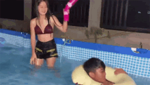 a woman in a bikini is spraying a man in a swimming pool