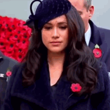 a close up of a woman wearing a hat and a coat with a poppy pin in her hair .