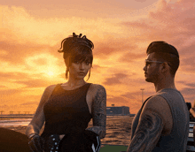 a man and a woman standing next to each other in front of a sunset