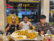 three men sitting at a table with a pizza in front of a sign that says 6 $ i9