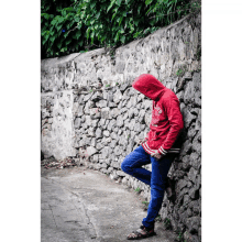 a man leaning against a stone wall wearing a red hoodie that says ' california ' on it