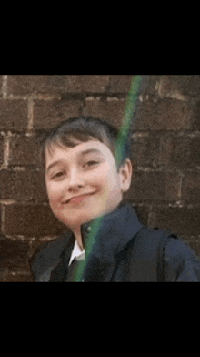 a young boy with a backpack is smiling in front of a brick wall .