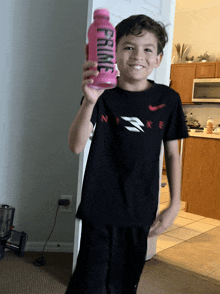 a boy in a black nike shirt holds up a pink bottle that says prime