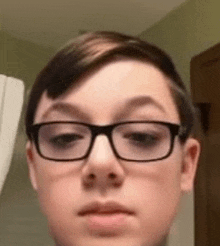 a young boy wearing glasses is looking at the camera in a bathroom .