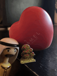 a red heart with camel written on it sits on a table next to a figurine