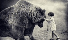 a little girl petting a large bear 's face in a black and white photo .