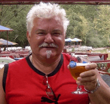 a man in a red shirt holding a glass of efes beer