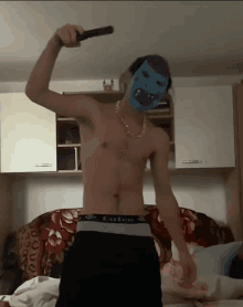 a shirtless man holding a microphone with a blue mask on his head