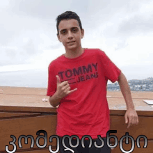 a young man wearing a red tommy jeans t-shirt stands on a balcony