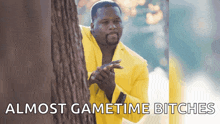 a man in a yellow suit is peeking out from behind a tree with the words " almost gametime bitches " below him