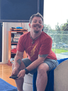 a man wearing a red shirt with a lightning bolt on it smiles