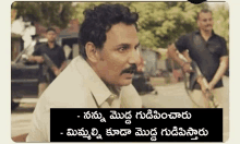 a man with a mustache is standing in front of a car with a caption in a foreign language .